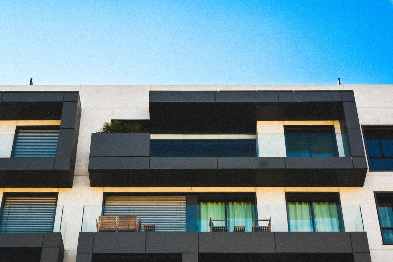 Minimalist apartment facade with glass balconies against a clear blue sky.